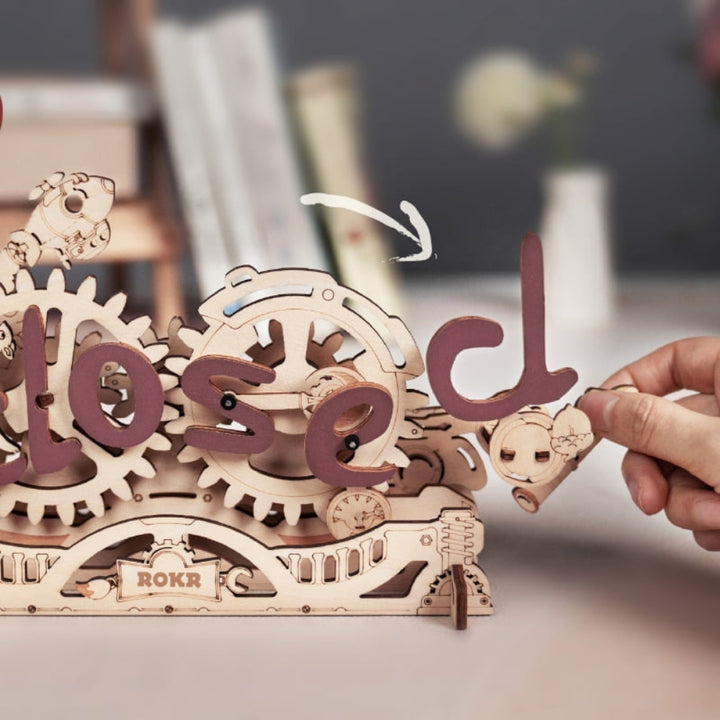 Wooden mechanical model with gears spelling 'closed' on a blurred background