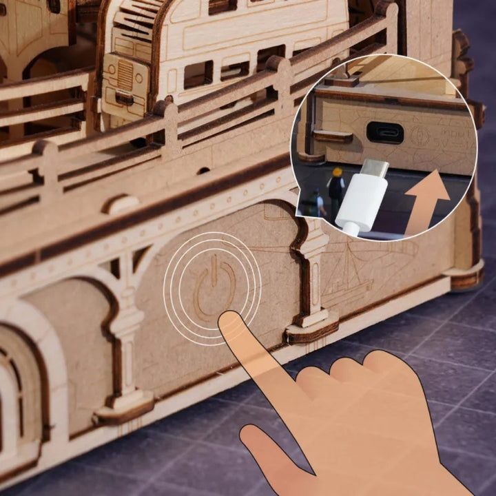 Wooden model train set with a hand pointing to a control panel, showing a close-up of the control buttons.